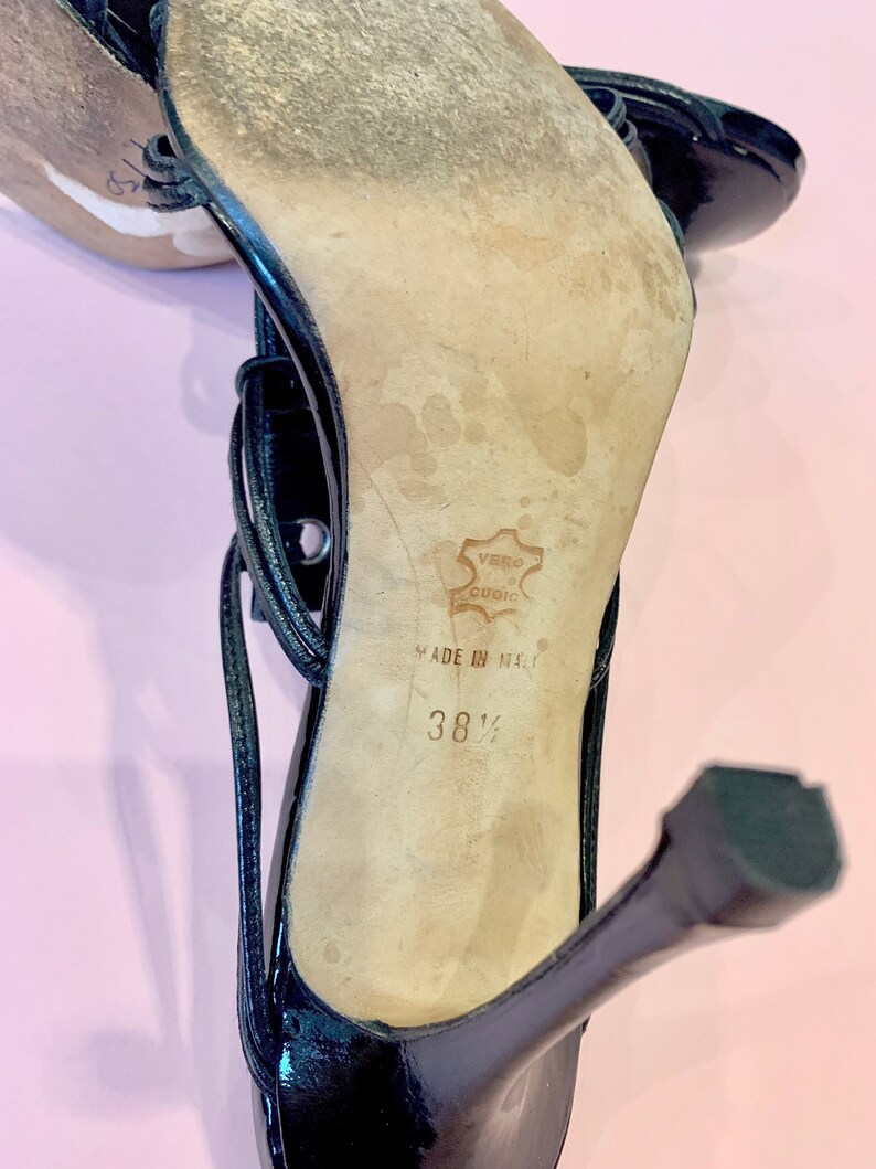 May include: Black leather high-heeled sandals with a buckle closure and a strap across the foot. The sandals are made in Italy and are size 38 1/2.