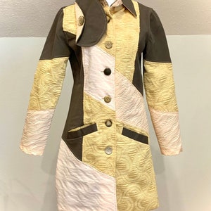 Puede incluir: Una chaqueta larga de manga larga, de estilo patchwork, en colores marrón, beige y rosa. La chaqueta tiene un cuello que se puede llevar subido o bajado, y se cierra con botones.