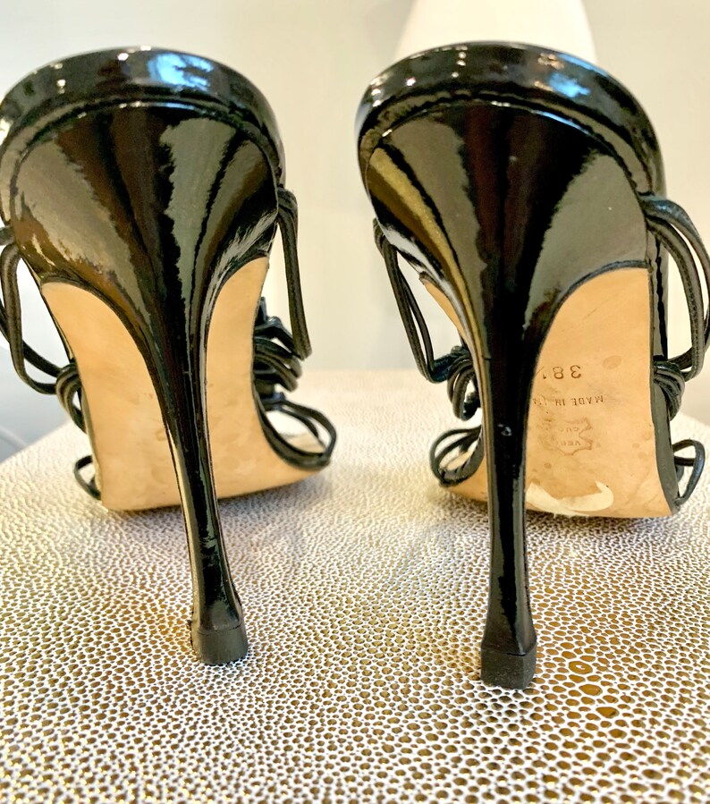 May include: Black patent leather high heeled sandals with a strappy design. The sandals have a thin heel and are made in Italy. The size is 38.