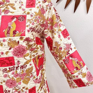 Pode incluir: Uma blusa de cor creme com estampa floral rosa e dourada. A estampa apresenta figuras estilizadas, flores e caracteres japoneses.