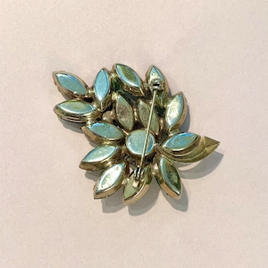 Pode incluir: Um broche dourado com um grupo de strass transparentes e iridescentes em um design floral.