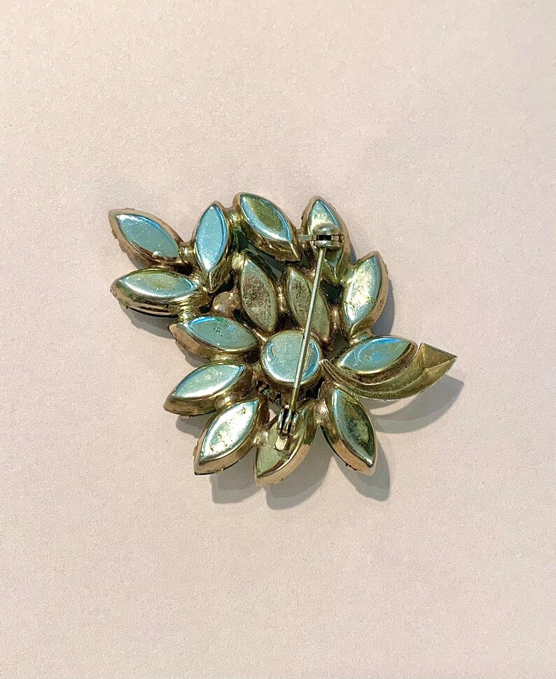 Pode incluir: Um broche dourado com um grupo de strass transparentes e iridescentes em um design floral.