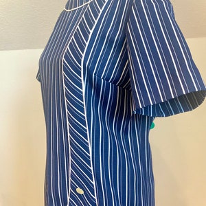 Pode incluir: Um vestido de riscas azuis e brancas com acabamento branco e três botões no lado. O vestido tem manga curta e decote redondo.