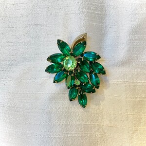 Pode incluir: Um broche vintage com um grupo de strass facetados verdes e verde claro em um design floral.