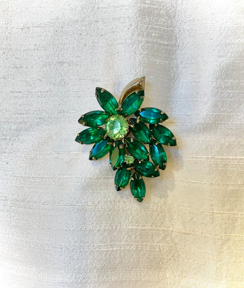 Pode incluir: Um broche vintage com um grupo de strass facetados verdes e verde claro em um design floral.