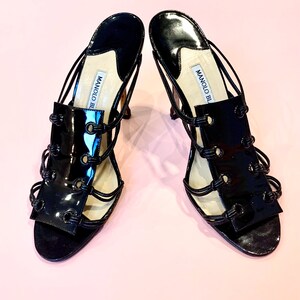 May include: A pair of black patent leather heeled sandals with a strappy design and the text "MANOLO BLAHNIK" on the straps.