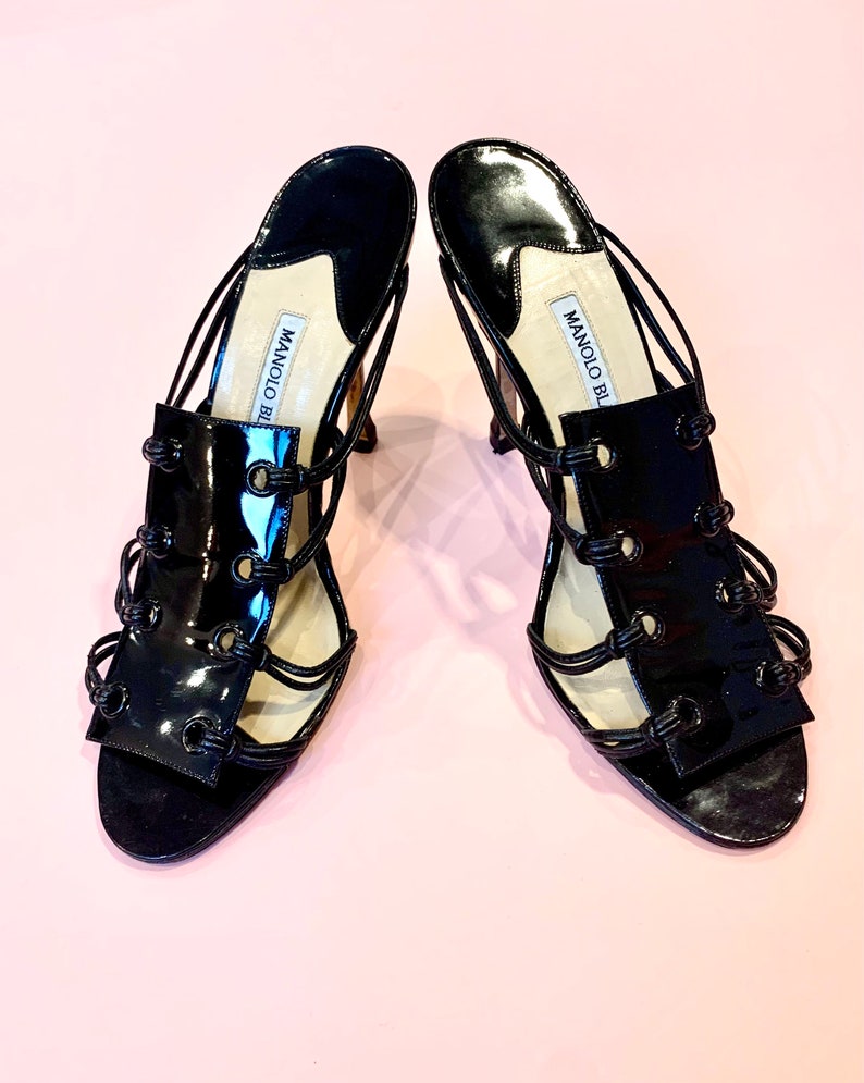May include: A pair of black patent leather heeled sandals with a strappy design and the text "MANOLO BLAHNIK" on the straps.