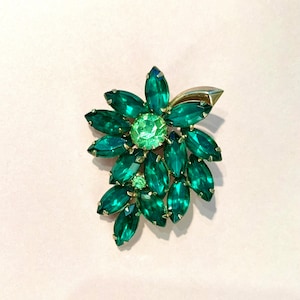 Pode incluir: Um broche verde e dourado com um grupo de strass em forma de marquise. O broche tem a forma de uma flor com um strass verde central.