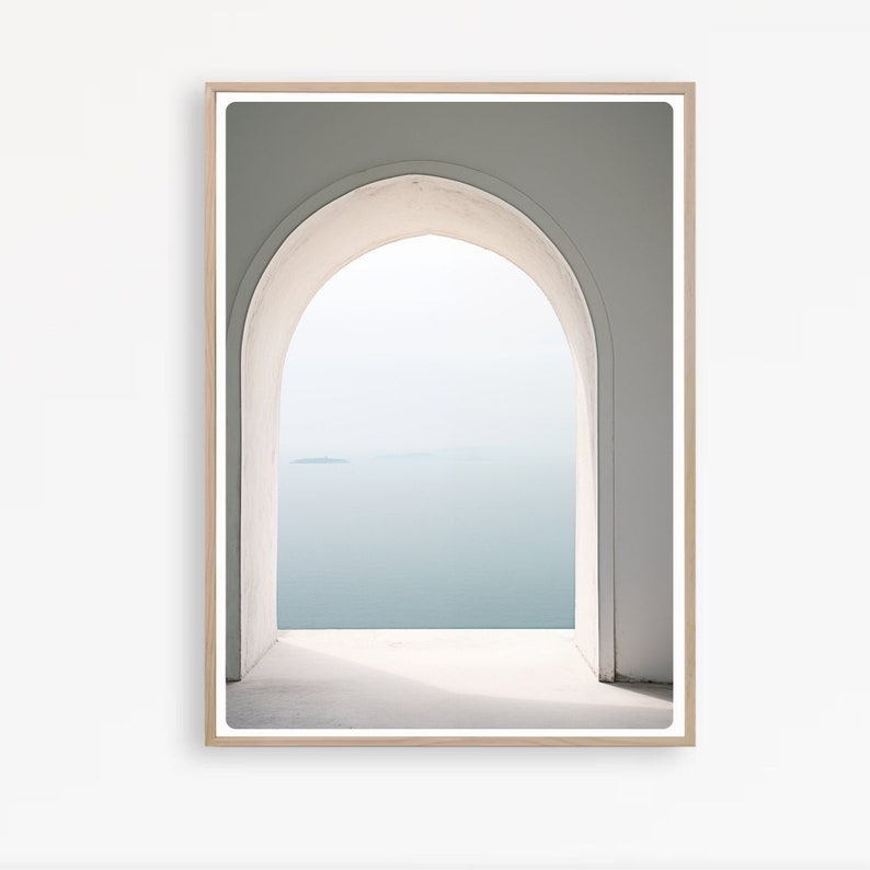 May include: A white archway with a view of a blue body of water and a small island in the distance. The archway is framed by a light wood frame.