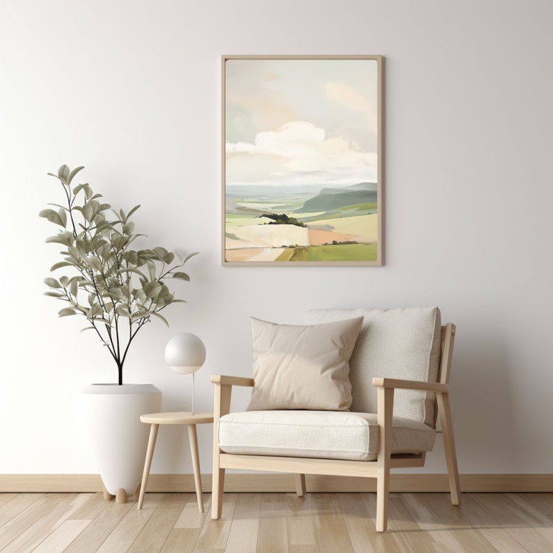 Puede incluir: Una pintura abstracta de paisaje enmarcada con un cielo azul claro, nubes blancas y colinas verdes y marrones. La pintura est&aacute; colgada en una pared blanca sobre un sill&oacute;n de madera clara con un coj&iacute;n blanco.