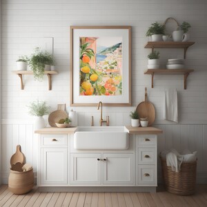 May include: A white farmhouse kitchen sink with a gold faucet, a white cabinet with drawers, and a framed watercolor painting of a Mediterranean landscape with citrus trees.