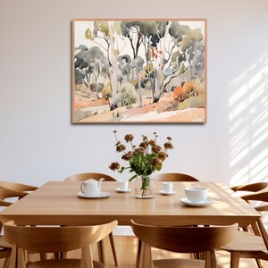 May include: A watercolor painting of a forest scene with tall trees and a light brown background. The painting is framed in a light wood frame and is hanging on a white wall above a wooden table with chairs.