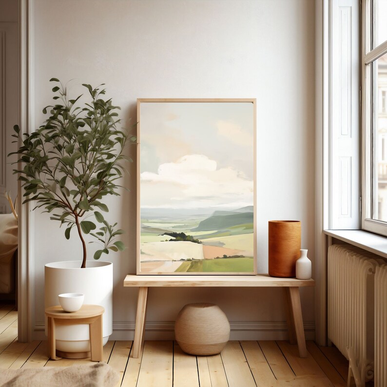 Puede incluir: Una pintura de paisaje enmarcada que representa una colina verde ondulada con una nube blanca en el cielo. La pintura est&aacute; colgada en una pared blanca en una habitaci&oacute;n con un banco de madera y una planta en maceta.
