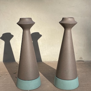 May include: Two brown ceramic candle holders with teal bases. The candle holders are cone-shaped with a wide opening at the top.