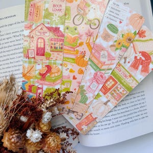 May include: Four rectangular bookmarks featuring autumn-themed illustrations including a library building, a frog reading, a bicycle, pumpkins, sunflowers, stacks of books, and text such as Quiet Please, Book Lover, and To Do: Read Books.