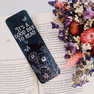 May include: A black bookmark with white floral designs and butterflies. The bookmark has the text "It's a good day to read" in white lettering.