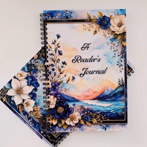 May include: A blue and white floral design journal with the title "A Reader's Journal" on the cover. The journal has a watercolor background with a mountain range and a lake.