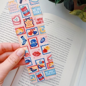 Puede incluir: Un marcap&aacute;ginas rectangular con un fondo rosa y varios dise&ntilde;os de sellos postales. Los sellos presentan im&aacute;genes de comida, corazones y textos como "Everyone Deserves Sunshine" y "We Didn't Even Kiss."