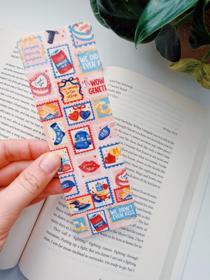Puede incluir: Un marcap&aacute;ginas rectangular con un fondo rosa y varios dise&ntilde;os de sellos postales. Los sellos presentan im&aacute;genes de comida, corazones y textos como "Everyone Deserves Sunshine" y "We Didn't Even Kiss."