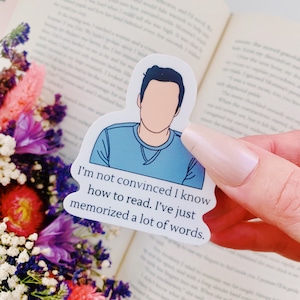 May include: A white sticker with a blue cartoon illustration of a person and the text "I'm not convinced I know how to read. I've just memorized a lot of words."
