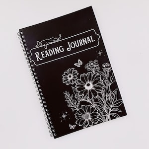 May include: Black spiral bound journal with the text "Reading Journal" in white lettering. The cover features a white silhouette of a cat, flowers, and butterflies.
