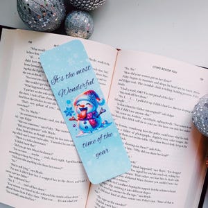 May include: A blue bookmark with a snowman illustration. The snowman is wearing a blue and white hat and scarf. The bookmark has the text "It's the most Wonderful time of the year" on it.