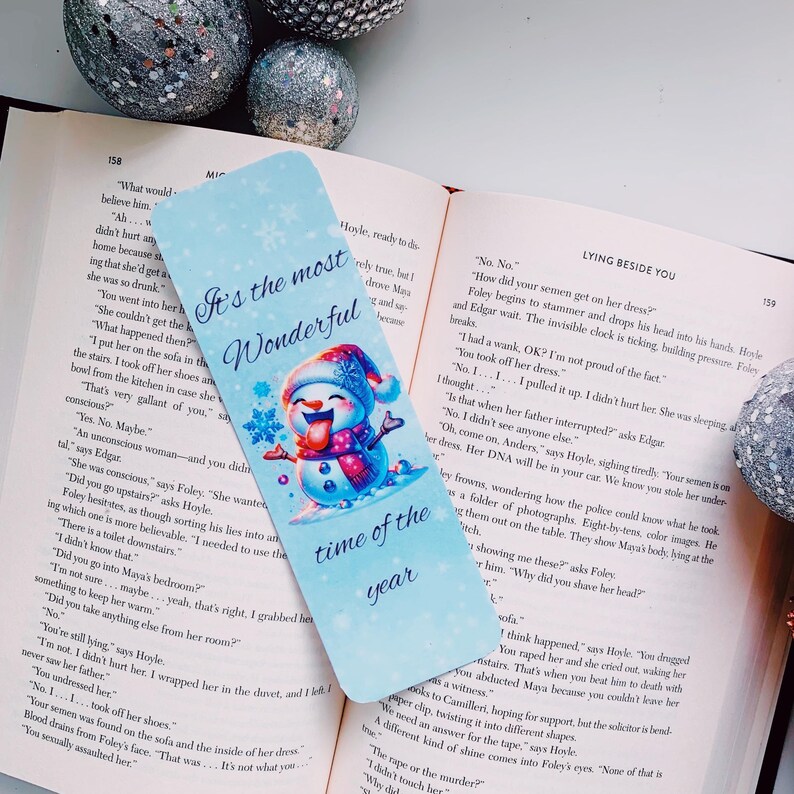 May include: A blue bookmark with a snowman illustration. The snowman is wearing a blue and white hat and scarf. The bookmark has the text "It's the most Wonderful time of the year" on it.