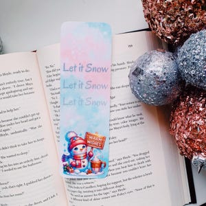 May include: A winter-themed bookmark featuring a snowman holding a mug with the text "Warm Wishes". The background is a watercolor-style design with the text "Let it Snow" repeated three times.