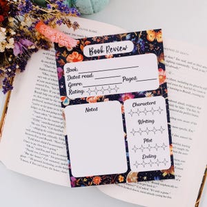 May include: A printable book review tracker with a floral design. The tracker has sections for the book title, author, genre, dates read, rating, notes, characters, writing, plot, and ending. The tracker is decorated with stars, butterflies, and moons.