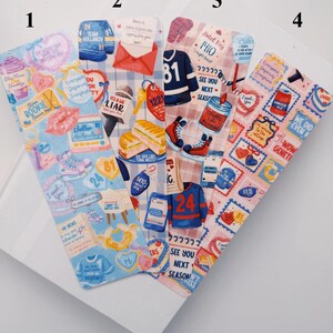 Puede incluir: Cuatro marcadores decorativos con varios dise&ntilde;os. Uno presenta un tema azul y rosa con texto como "Rookie" y "Boston". Otro tiene un tema rojo y blanco con una carta y un s&aacute;ndwich. El tercero tiene un tema de hockey con una camiseta y patines. El &uacute;ltimo tiene un tema rosa y rojo con sellos.