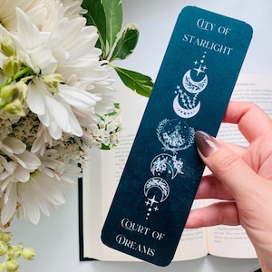 Puede incluir: Un marcap&aacute;ginas azul oscuro con texto blanco e ilustraciones. El texto dice "City of Starlight" y "Court of Dreams". Las ilustraciones son de lunas, estrellas y hojas.