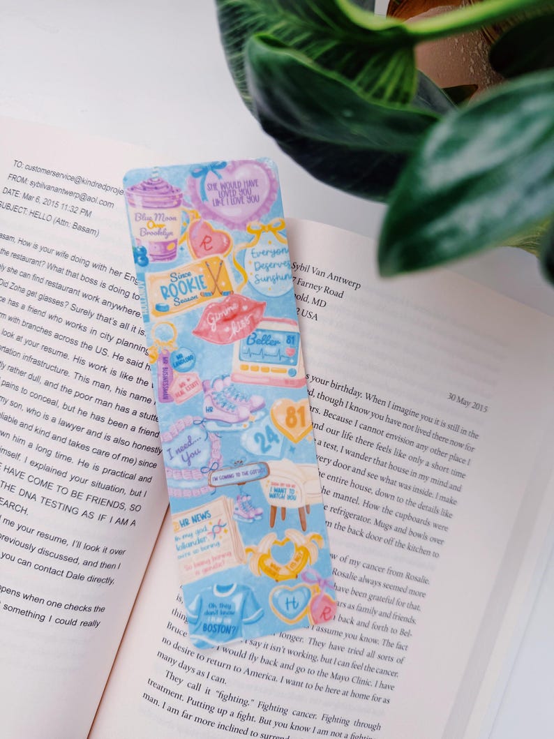 Puede incluir: Un marcap&aacute;ginas colorido con varias ilustraciones y texto, incluyendo corazones, una camiseta de Boston y las palabras "I need you". El marcap&aacute;ginas est&aacute; colocado en un libro abierto.