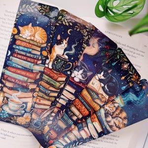 May include: A collection of whimsical cat-themed bookmarks. Each bookmark features a different cat illustration, set against a backdrop of books, stars, and celestial elements. The bookmarks have titles like "Marmalade Dreams" and "Feline Folklore".