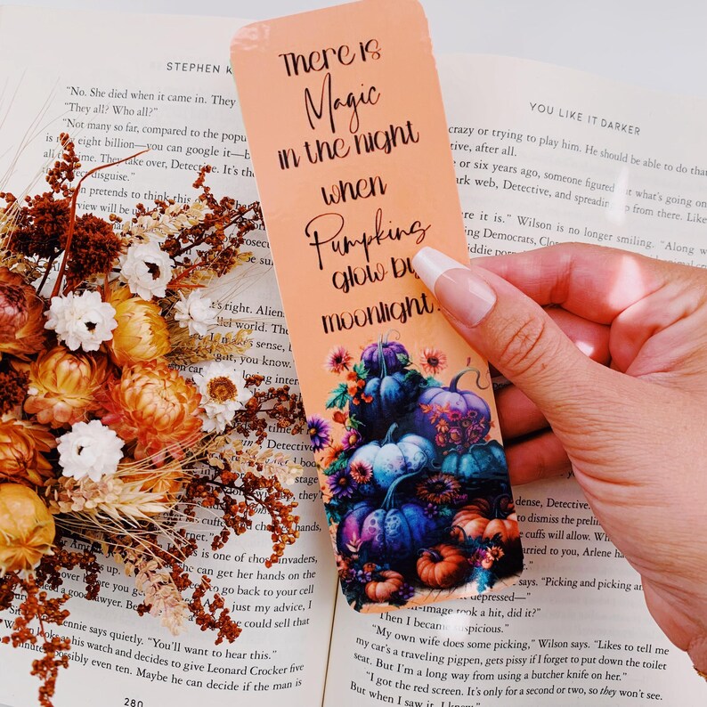 K&ouml;nnte beinhalten: Ein pfirsichfarbener Lesezeichen mit dem Text "There is Magic in the night when Pumpkins glow by moonlight." Das Lesezeichen zeigt eine farbenfrohe Illustration von K&uuml;rbissen mit Blumen und Bl&auml;ttern.