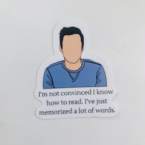 May include: A sticker featuring a cartoon illustration of a person with a blue shirt and the text "I'm not convinced I know how to read. I've just memorized a lot of words."