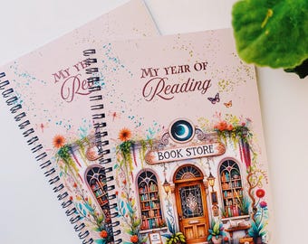 May include: Two spiral-bound notebooks with the text "My Year of Reading" on the cover. The cover features a detailed illustration of a bookstore with floral accents, a turtle, and the words "Book Store".