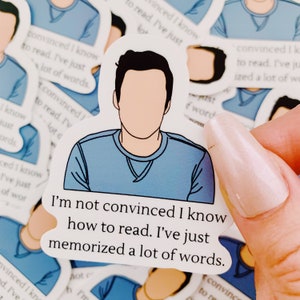 May include: A blue sticker with a cartoon illustration of a person with the text "I'm not convinced I know how to read. I've just memorized a lot of words."