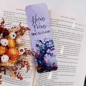 K&ouml;nnte beinhalten: Ein lila und blaues Lesezeichen mit einem fantasievollen Baumdesign und dem Text "Hocus Focus Time to Focus". Der Baum ist von bunten Blumen und Bl&auml;ttern umgeben.