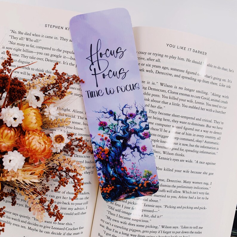 K&ouml;nnte beinhalten: Ein lila und blaues Lesezeichen mit einem fantasievollen Baumdesign und dem Text "Hocus Focus Time to Focus". Der Baum ist von bunten Blumen und Bl&auml;ttern umgeben.