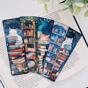 May include: Six colorful bookmarks featuring a cat sleeping on a stack of books. Each bookmark has a different color scheme and features a cat with different colored fur. The bookmarks are perfect for book lovers and cat enthusiasts.
