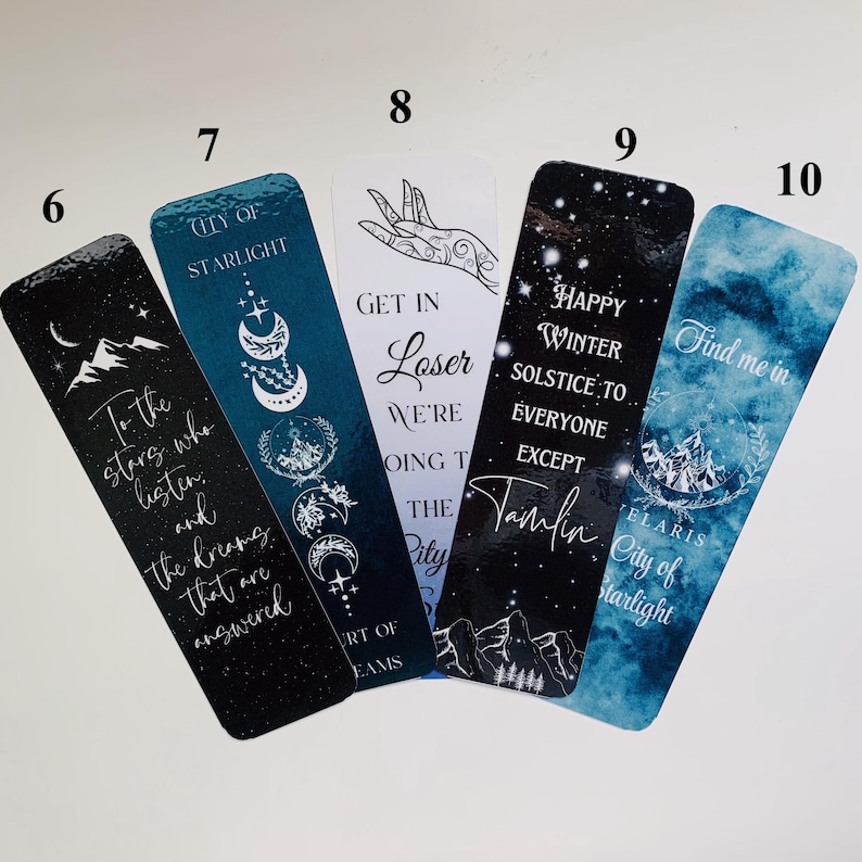 Puede incluir: Conjunto de seis marcap&aacute;ginas con diferentes dise&ntilde;os y citas. Los marcap&aacute;ginas son todos rectangulares y tienen una combinaci&oacute;n de colores azul y negro. Las citas en los marcap&aacute;ginas incluyen "To the stars who listen", "Get in Loser We're Going to the City", "Happy Winter Solstice to Everyone Except Tamlin", y "Find me in Elaris City of Starlight".