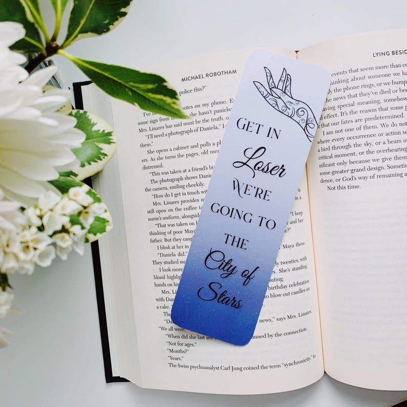 Puede incluir: Un marcap&aacute;ginas azul y blanco degradado con una ilustraci&oacute;n de mano y el texto "Get in Loser We're Going to The City of Stars".