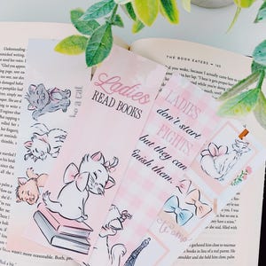 May include: A collection of pink and white bookmarks featuring illustrations of a cat with a bow, books, and the Eiffel Tower. Text includes "Ladies Read Books" and "Ladies don't start fights but they can finish them."