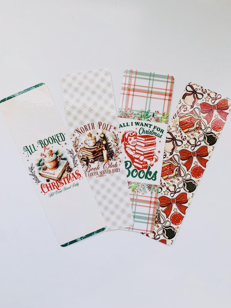May include: Four Christmas-themed bookmarks with festive designs. One bookmark features a cocoa illustration with the text "All Booked for Christmas". Another says "North Pole Book Club". The third says "All I Want for Christmas is Books". The last has bows and gift boxes.