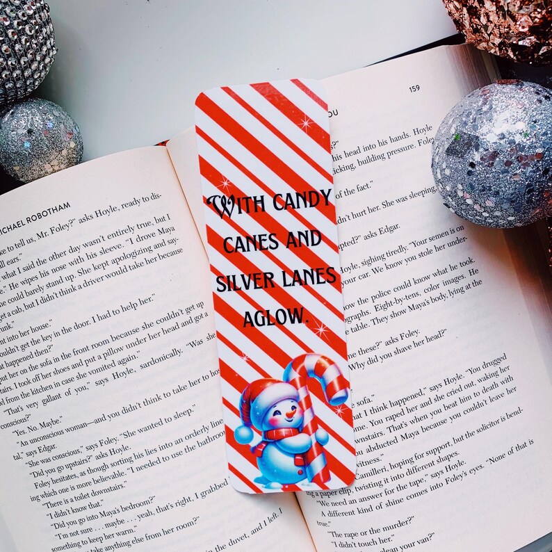 May include: A red and white striped bookmark with a snowman holding a candy cane. The bookmark has the text "With Candy Canes and Silver Lanes Aglow".