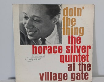 May include: A vintage vinyl record cover featuring a black and white photo of Horace Silver, a jazz musician. The cover is white with red and orange text that reads "doin' the thing the horace silver quintet at the village gate". The Blue Note record label is visible in the bottom left corner.