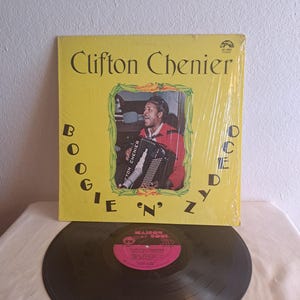 May include: A vintage vinyl record album by Clifton Chenier, titled "Boogie 'n' Zydeco". The album cover is yellow with a photo of Chenier playing an accordion. The record itself is black with a pink label.