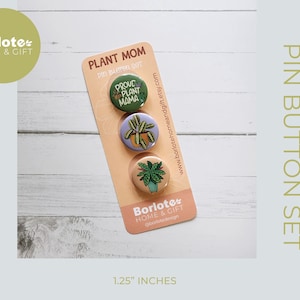 May include: A set of three 1.25 inch diameter button pins featuring plant-themed designs. The pins are on a card with the text "Plant Mom Pin Button Set" and "Prove Plant Mama".