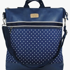May include: A blue and white polka dot backpack with a navy blue faux leather top flap. The flap has a brown leather patch with the text "ISABELLA MYA" in white.