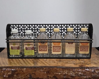 Estante para especias de metal negro vintage con botellas para aromatizantes y extractos. Decoración rústica y campestre.